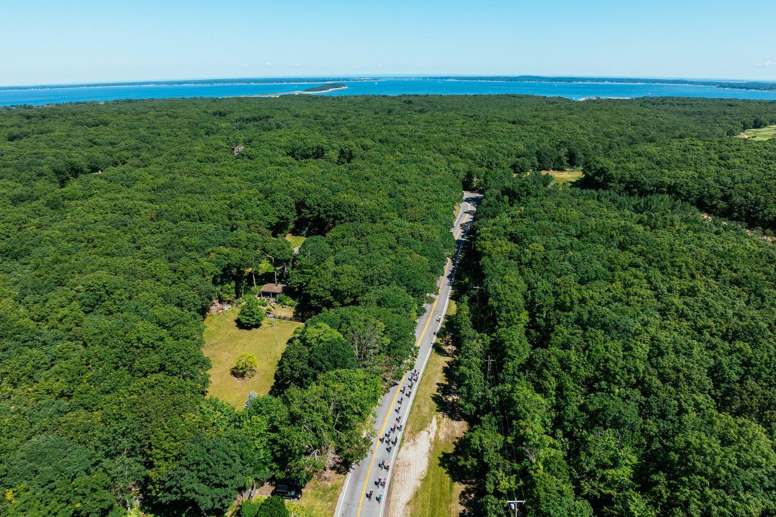 Aerial view of a cycling group ride through Hamptons woodland toward the bay
